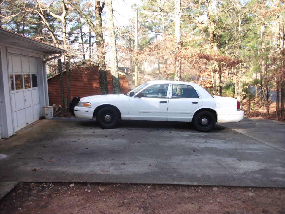 white sedan parked next to a garage, trees in background