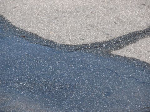 1968 Ford Mustang - A puddle reflects the sky on a section of cracked asphalt.