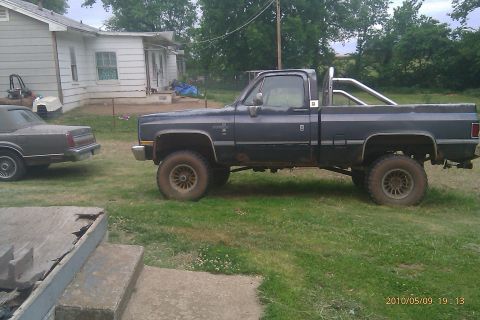 2000 Mercury Grand Marquis - A lifted pickup truck and a sedan sit in a grassy yard next to a house.
