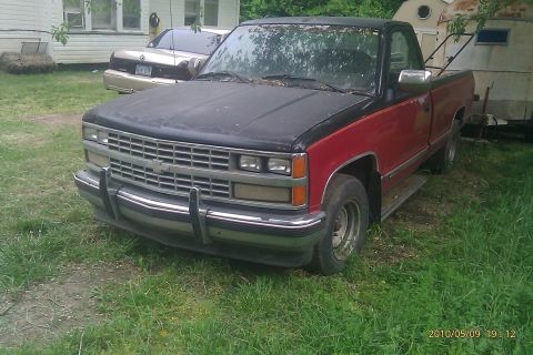 2000 Mercury Grand Marquis - A red and black pickup truck is parked in a grassy yard, with a sedan visible behind it.