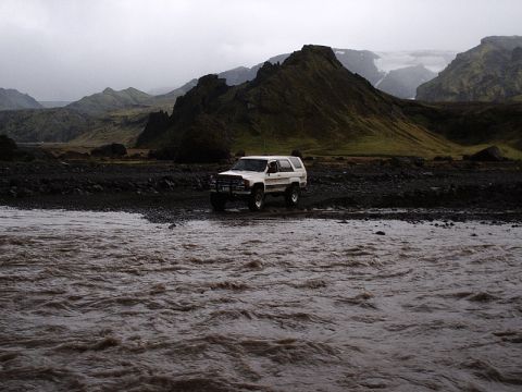 1996 Ford Bronco - White SUV parked on gravel near a river with mountains in the background.