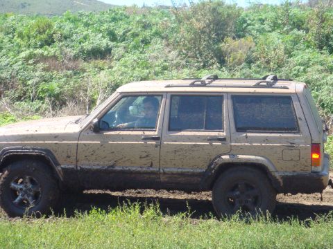 1992 Ford Bronco - Mud-splattered Jeep Cherokee XJ navigates an off-road trail.