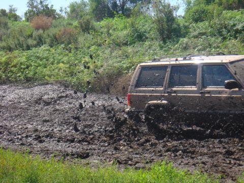 1992 Ford Bronco - This tan SUV is navigating a challenging muddy terrain, with water and mud spraying around it.