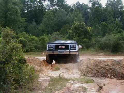 1990 Ford Bronco - A GMC pickup truck navigates an off-road course with dirt mounds.