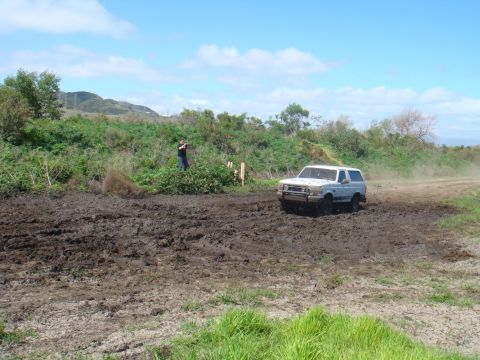 1992 Ford Bronco - A 1992 Ford Bronco navigates a challenging muddy terrain under a partly cloudy sky.