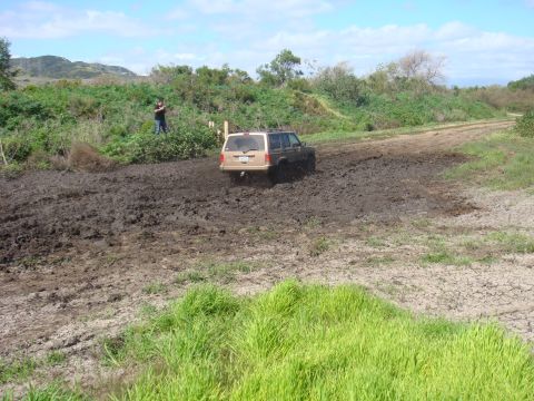 1992 Ford Bronco - A Jeep Cherokee XJ navigates a muddy trail with a bystander watching.