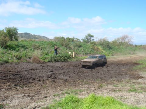 1992 Ford Bronco - A Jeep Cherokee XJ navigates a challenging muddy terrain under a partly cloudy sky.
