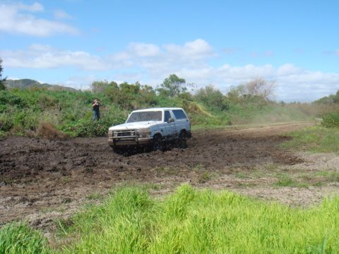 1992 Ford Bronco - A white 1992 Ford Bronco navigates a muddy off-road course under a partly cloudy sky.