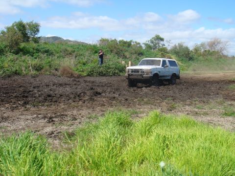 1992 Ford Bronco - 1992 Ford Bronco navigating a challenging muddy terrain under a partly cloudy sky.