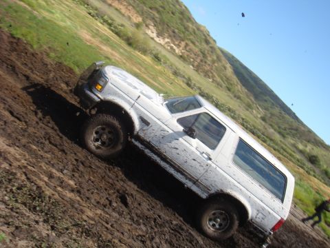 1992 Ford Bronco - White 1992 Ford Bronco navigates a challenging muddy terrain on a hillside.