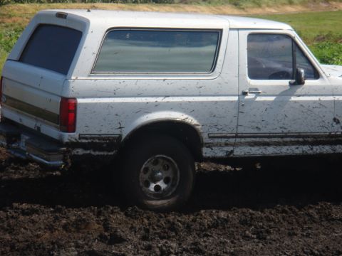 1992 Ford Bronco - White Ford Bronco is stuck in mud, showing its side profile.