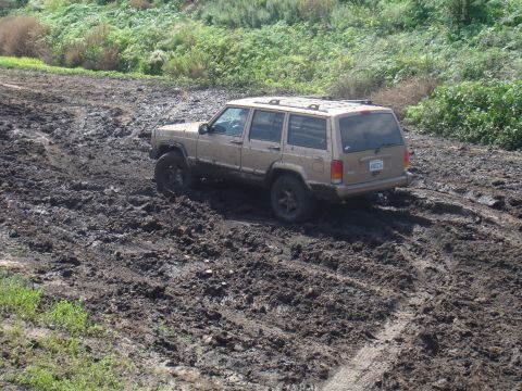 1992 Ford Bronco - A tan Jeep Cherokee XJ navigates a muddy off-road trail.