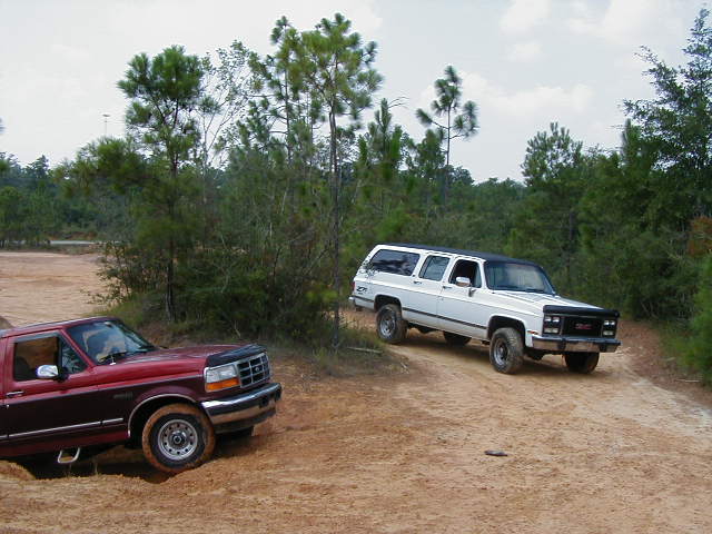 Red Ford pickup truck and white GMC Suburban on dirt road
