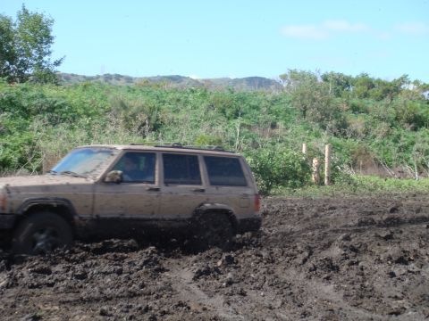 1992 Ford Bronco - A tan Jeep Cherokee XJ navigates through deep mud, its tires struggling for traction.