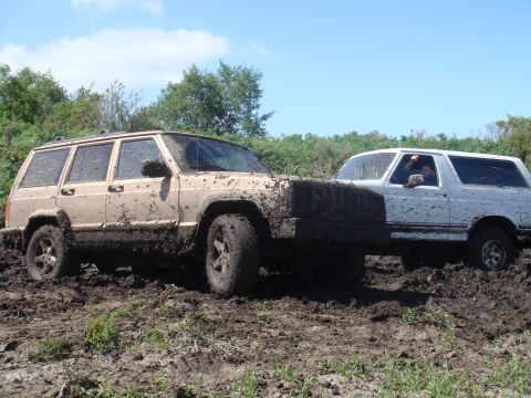 1992 Ford Bronco - Two off-road vehicles are covered in mud after navigating a difficult trail.