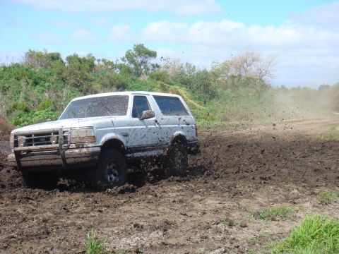 1992 Ford Bronco - A white Ford Bronco navigates a muddy off-road course, sending dirt flying.