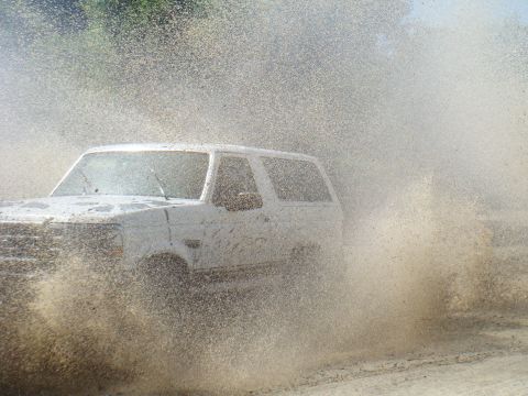 1992 Ford Bronco - A white 1992 Ford Bronco kicks up a large spray of mud and water as it drives through a muddy area.