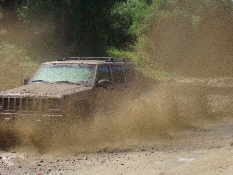 1992 Ford Bronco - Jeep Cherokee XJ navigating a muddy trail, kicking up a large spray.