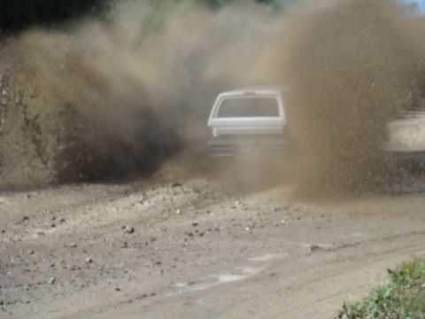 1992 Ford Bronco - A white SUV drives through a muddy area, creating a large spray of dirt and water.