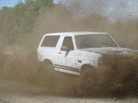 1992 Ford Bronco - A white 1992 Ford Bronco kicks up a large amount of mud as it drives off-road.
