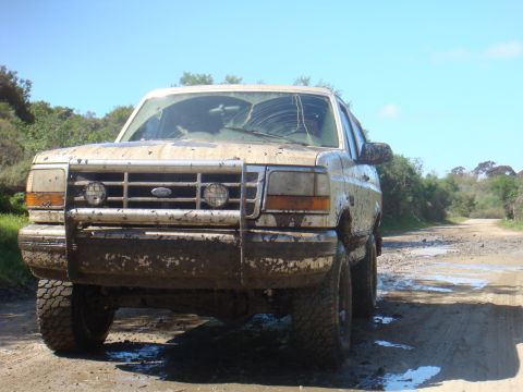 1992 Ford Bronco - Muddy 1992 Ford Bronco navigates a dirt road, suggesting off-road use.