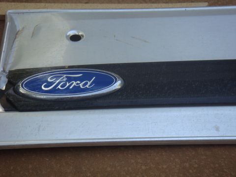 1992 Ford Bronco - A Ford emblem is shown on a silver trim piece, possibly from a vehicle's exterior.