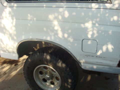 1992 Ford Bronco - Close-up of a white Ford Bronco's side, showing the rear wheel and fuel door with tree shadows.