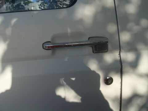 1992 Ford Bronco - Detail shot of a vehicle's door handle and lock, with dappled sunlight creating shadows on the surface.