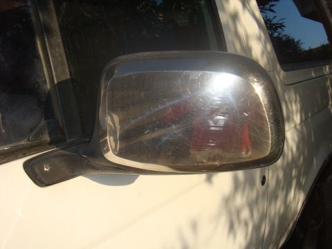 1992 Ford Bronco - A close-up view of a white vehicle's side mirror and door panel shows signs of wear and tear.