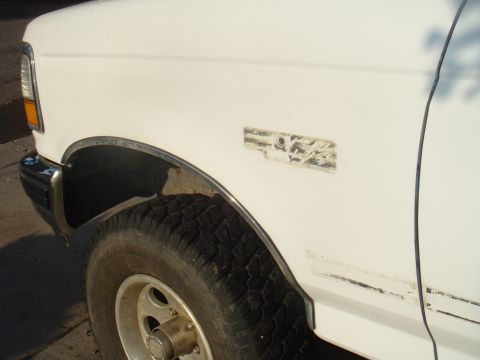 1992 Ford Bronco - Close-up of a white truck's front fender and tire, showing a worn decal.