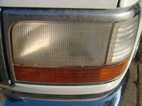 1992 Ford Bronco - Close-up of the front headlight and chrome grille of a white 1992 Ford Bronco.