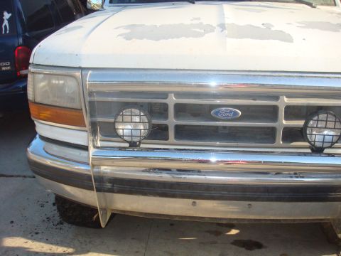 1992 Ford Bronco - The front grille and headlights of a white Ford truck, possibly a 1992 Bronco, are visible with a chrome bumper and auxiliary lights.