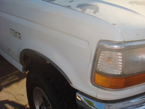 1992 Ford Bronco - Close-up of the front corner of a white 1992 Ford Bronco, showing the fender, headlight, and chrome bumper detail.