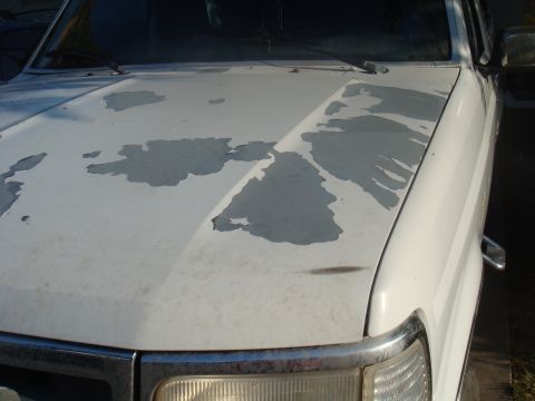 1992 Ford Bronco - The hood of a white 1992 Ford Bronco shows significant paint damage, revealing the primer underneath.