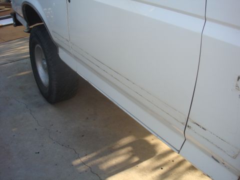 1992 Ford Bronco - The side panel of a white 1992 Ford Bronco shows minor scuffs and a prominent trim line.