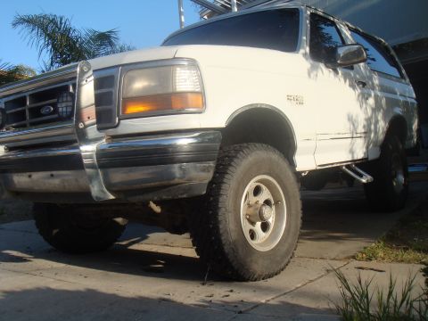 1992 Ford Bronco - This white Ford Bronco is shown from a low front angle, highlighting its lifted suspension and off-road tires.