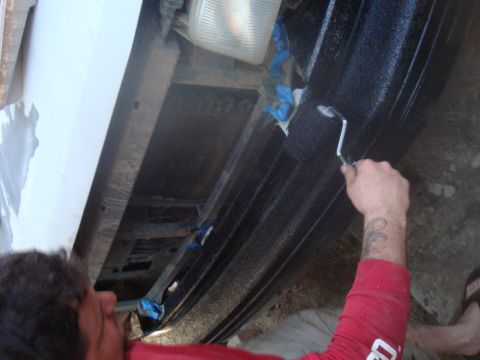 1992 Ford Bronco - A person applies a protective coating to the frame of a vehicle, likely for rust prevention or sound dampening.