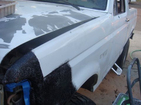 1992 Ford Bronco - A white truck's fender is being sprayed with black undercoating, with blue tape protecting adjacent areas.