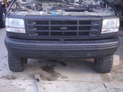 1992 Ford Bronco - This Ford truck's front end is visible, with the hood up and large tires on the ground.