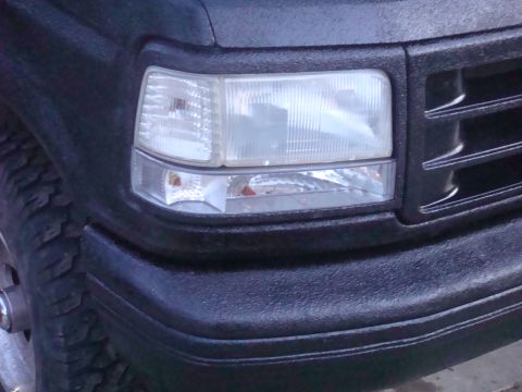 1992 Ford Bronco - Close-up of the front corner of a 1992 Ford Bronco, showing the headlight and textured bumper.