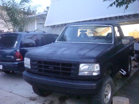 1992 Ford Bronco - Black 1992 Ford Bronco in front of a garage, with a dark SUV to its left.