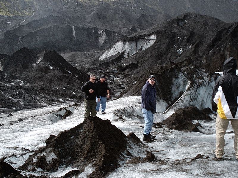 People standing on an ash-covered glacier among dark mountains