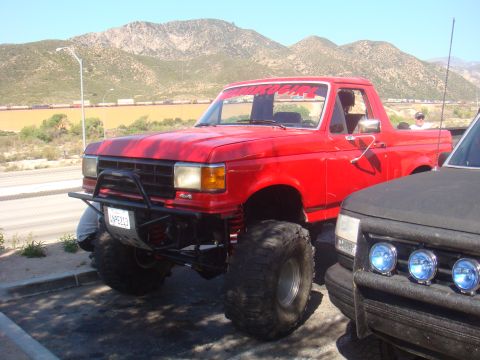 1992 Ford Bronco - This lifted 1992 Ford Bronco features oversized tires and a custom brush guard, parked next to another vehicle.