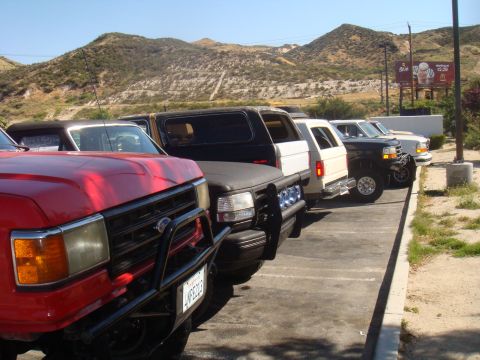 1992 Ford Bronco - Several Ford Broncos and F-Series trucks are parked in a lot with a mountainous backdrop.
