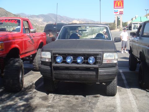 1992 Ford Bronco - A black Ford Bronco is parked in a lot with other vehicles, including a red pickup truck.