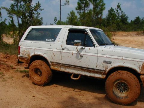1990 Ford Bronco - This white 1990 Ford Bronco is shown off-road, covered in mud, with its 3q-front view prominent.