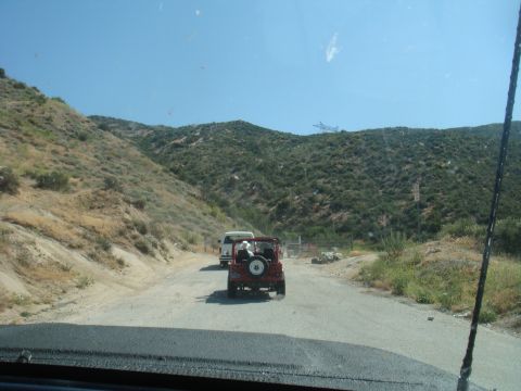 1992 Ford Bronco - Two vehicles travel down a dusty road through a mountainous, arid terrain under a clear blue sky.