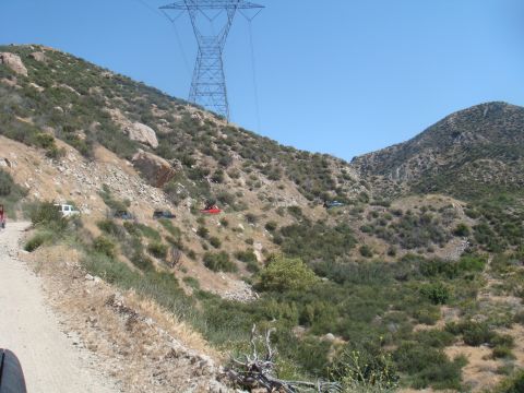 1992 Ford Bronco - Multiple vehicles traverse a mountain path, with a large power line tower visible against the clear blue sky.