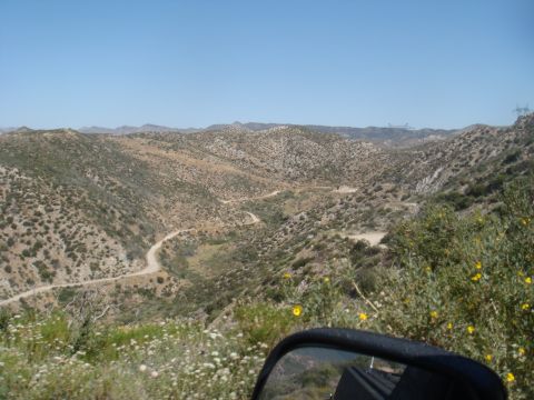 1992 Ford Bronco - A view from a vehicle shows a remote dirt road winding through arid hills, with wildflowers in the foreground.