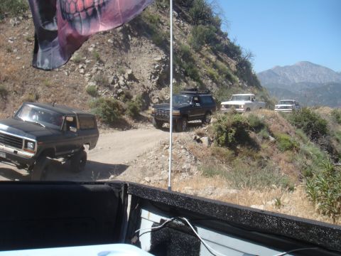 1992 Ford Bronco - Multiple vehicles navigate a dusty mountain trail under a clear blue sky.
